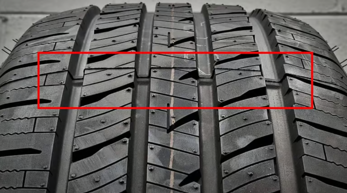 டயரின் உட்புறப் பள்ளங்களுக்குள் TWI (Tread Wear Indicator) குறியீட்டைக் காட்டும் ஒரு நெருக்கமான படம்.