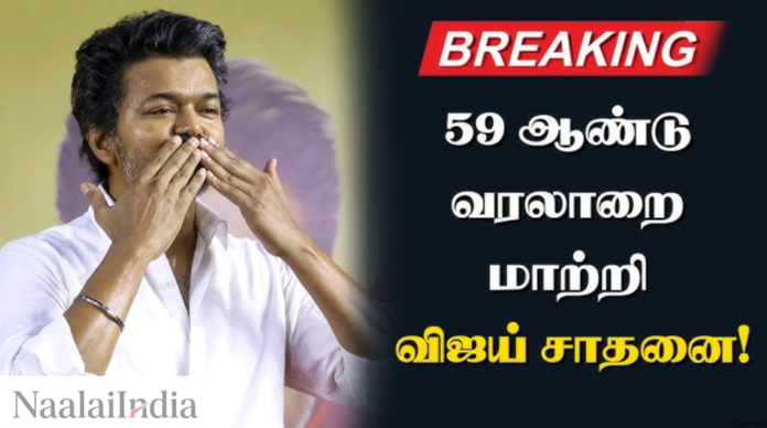 சினிமா நடிகர் விஜய், பிரம்மாண்டமான அரசியல் கூட்டத்தில் தொண்டர்கள் மத்தியில் கையை அசைத்து பிரசாரம் செய்கிறார்.